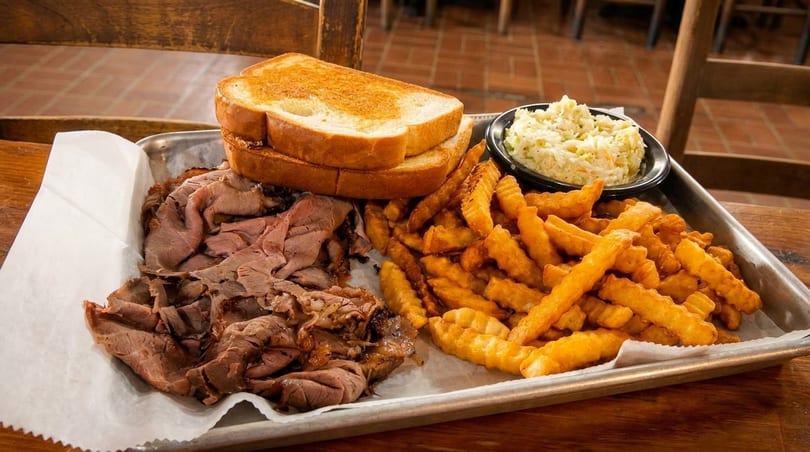 A metal tray with sliced roast beef, crinkle-cut fries, coleslaw, and toasted bread.